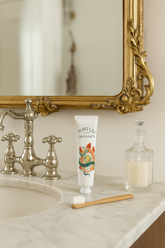 Luxury marble bathroom counter with Turtlee Organics toothpaste tube and wooden toothbrush beside a vintage gold mirror.